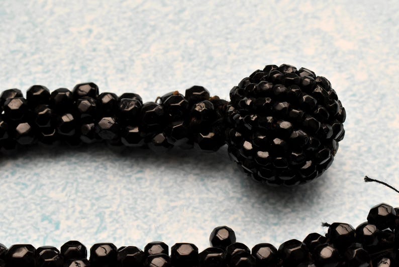 May include: A black beaded necklace with a large black bead at the end. The beads are small and round, and the necklace is made of a single strand.