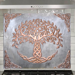 May include: A stainless steel range hood with a copper Celtic tree of life design backsplash. The backsplash is mounted above a stainless steel stove with a black hob.
