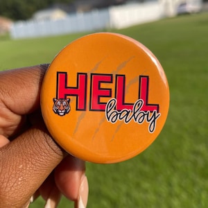 May include: Orange button with the words "HELL baby" in red and black lettering. A tiger graphic is on the left side of the word "HELL". The button has claw marks on the surface.