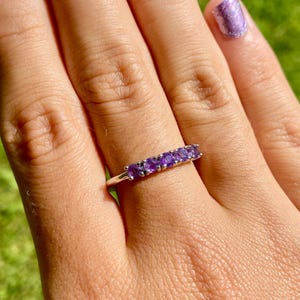 Könnte beinhalten: Ein Silberring mit einer Reihe von violetten Amethyststeinen.