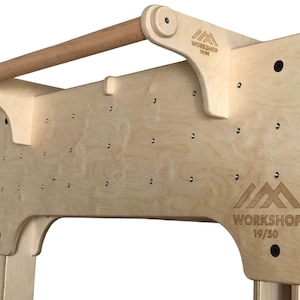 May include: A wooden pull-up bar mounted on a plywood wall with a logo that reads "WORKSHOP 19/50".