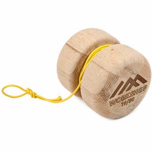 Könnte beinhalten: Ein helles Holz-Jojo mit einer leuchtend gelben Schnur, die um die Mitte gewickelt ist. Auf der Seite des Jojos befindet sich ein lasergraviertes Bergsymbol über dem Schriftzug WORKSHOP und der Nummer 19/50, was auf eine limitierte Auflage hinweist.