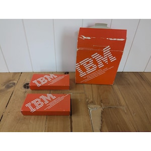 May include: An orange IBM box and two smaller boxes with the IBM logo in white. The boxes are on a wooden surface. The large box has a handle on top and text on the side.