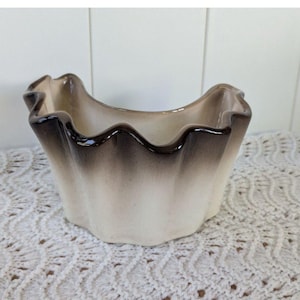May include: A ceramic planter with a wavy rim, featuring a gradient of colors from light beige to dark brown. The planter has a unique, scalloped edge and a glossy finish, suitable for small plants or decorative use.