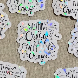 May include: A white sticker with iridescent glitter accents. The sticker features the text "Nothing Changes If Nothing Changes." in black cursive lettering.