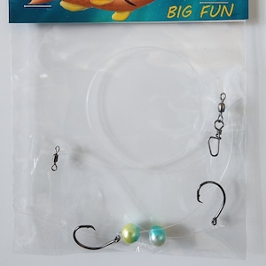 May include: A clear plastic bag containing a fishing rig with two green and blue beads, a hook, and a swivel. The bag has a header that says "Kids Rigs" with a cartoon fish and the text "little rigs BIG FUN".