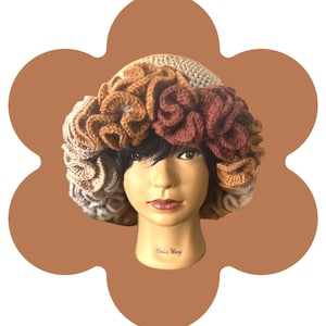 May include: A beige crochet hat with a floral design in shades of brown and tan. The hat is displayed on a mannequin head. The text "Hair Way" is visible on the mannequin's neck.