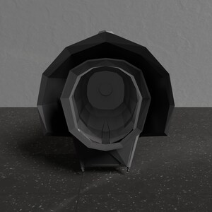 May include: A black, geometrically shaped object with a large, open, circular opening in the front. The object is sitting on a black, speckled surface.
