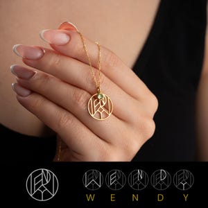 May include: Gold necklace with a circular pendant featuring a geometric design and a small green gemstone. The pendant is inscribed with the letters "W", "E", "N", "D", and "Y".