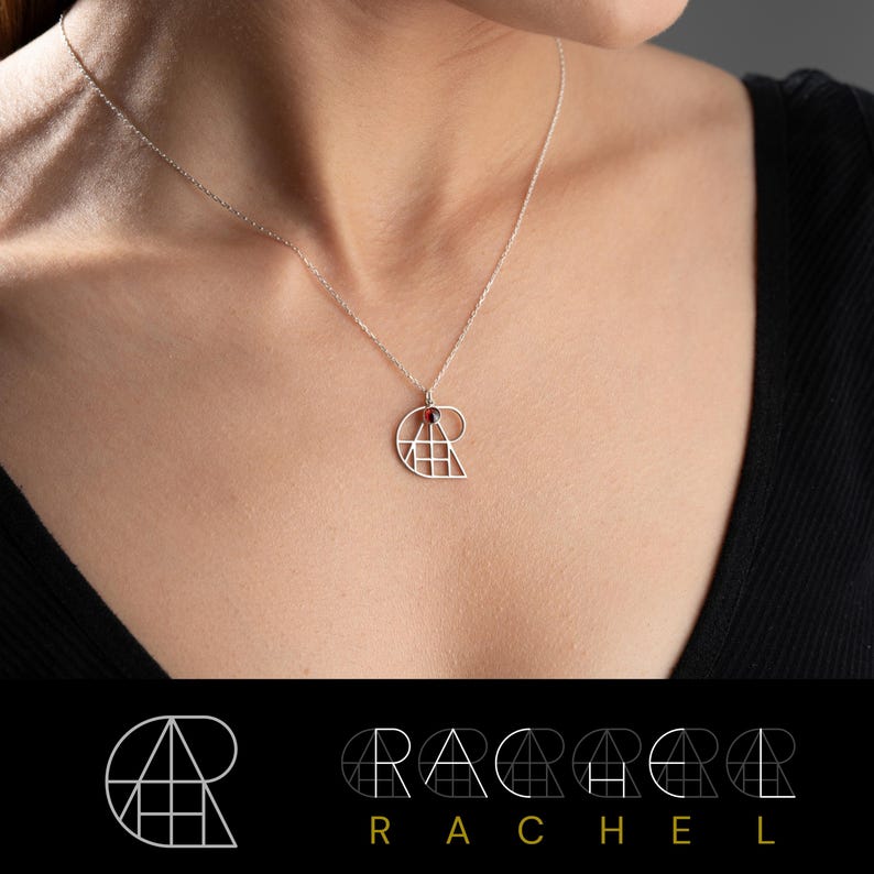 May include: A silver necklace with a geometric pendant featuring a red gemstone. The pendant is shaped like a spiral and is made up of triangles and squares. The necklace is on a model wearing a black shirt.