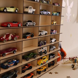 May include: A wooden shelf unit with multiple shelves, each holding a different toy car. The cars are in various colors, including red, blue, yellow, and green. The shelf unit is made of light brown wood and has a simple design.