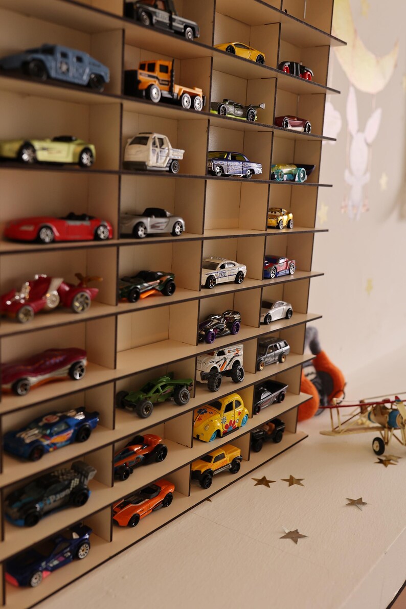 May include: A wooden shelf unit with multiple shelves, each holding a different toy car. The cars are in various colors, including red, blue, yellow, and green. The shelf unit is made of light brown wood and has a simple design.