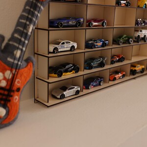 May include: A wooden shelf unit with multiple shelves, each holding a variety of toy cars. The cars are in different colors and styles, including red, blue, green, and black. The shelf unit is made of light wood and has a simple design.