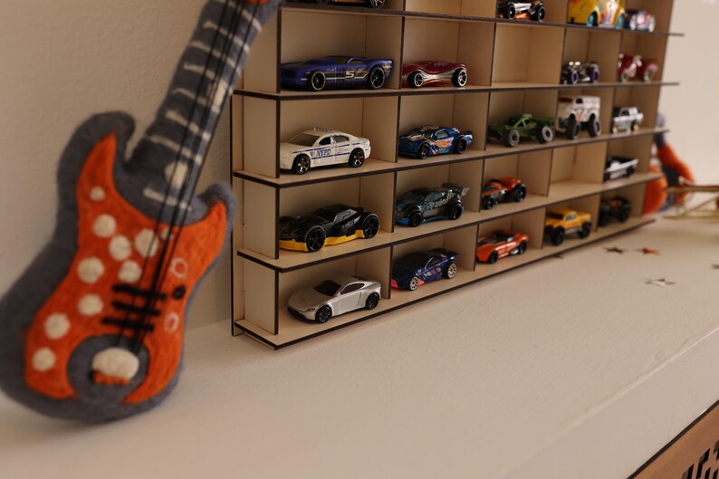 May include: A wooden shelf unit with multiple shelves, each holding a variety of toy cars. The cars are in different colors and styles, including red, blue, green, and black. The shelf unit is made of light wood and has a simple design.