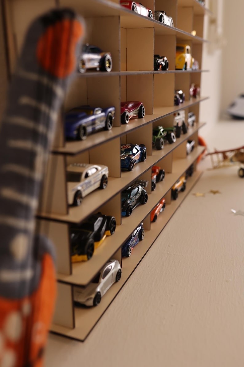 May include: A wooden toy car display shelf with multiple levels. The shelf is filled with toy cars in various colors, including red, blue, black, and silver.