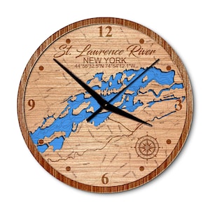 May include: A round wooden wall clock featuring a detailed map of the St. Lawrence River in New York, with blue water and black clock hands. The clock face includes the numbers 12, 3, 6, and 9, and a compass rose.