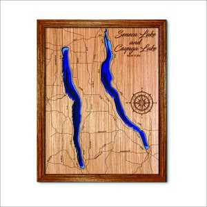 May include: A wooden map of Seneca Lake and Cayuga Lake in New York. The lakes are carved out of the wood and painted blue. A compass rose is in the lower right corner.