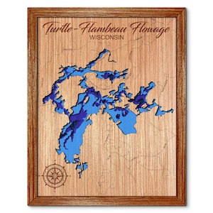 May include: A wooden map of Turtle-Flambeau Flowage in Wisconsin. The map is framed in a brown wood frame and features a compass rose in the lower left corner.
