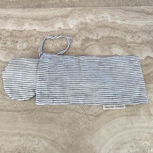 A soft ivory/black pinstriped sleep mask peeking out of its drawstring pouch, displayed on a kitchen counter.