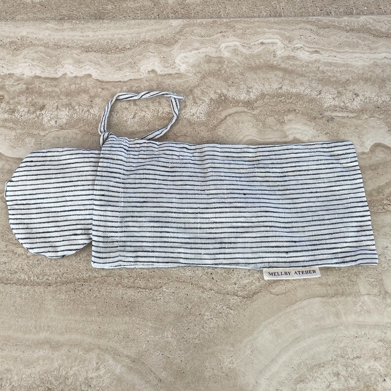 A soft ivory/black pinstriped sleep mask peeking out of its drawstring pouch, displayed on a kitchen counter.