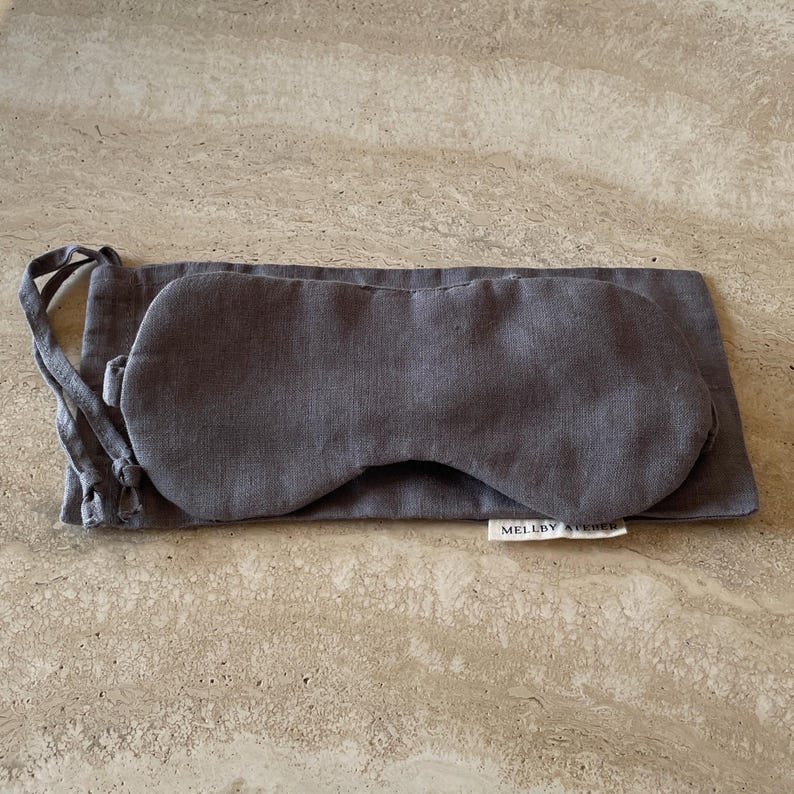 Linen sleep mask with its pouch in charcoal, displayed on a kitchen counter.