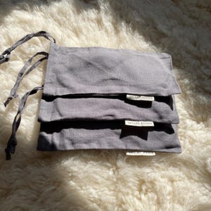 Three charcoal grey sleep masks in their drawstring pouches.