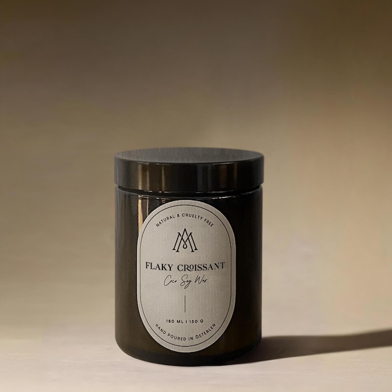 Amber glass candle jar labeled “Flaky Croissant” with coconut soy wax, minimalist apothecary-style design, photographed in warm natural light.