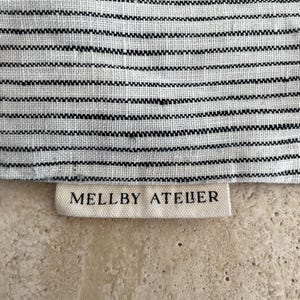 Closeup of the Mellby Atelier tag on a soft ivory/black pinstripes sleep mask drawstring bag.