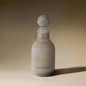 Puede incluir: Una botella de vidrio transparente con una superficie texturizada y un tapón de vidrio. La botella tiene una etiqueta que dice "MELT" y "OTHER" con un logotipo de dos triángulos.