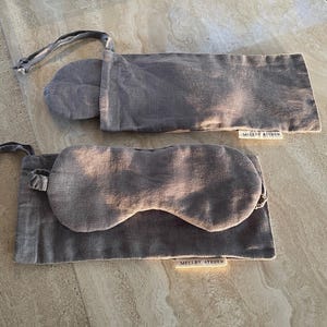 Two Mellby Atelier linen sleep masks with their pouch in charcoal, displayed on a kitchen counter