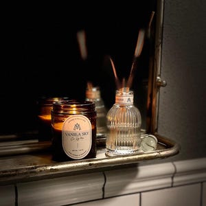 Lit amber jar vanilla scented candle on bathroom shelf paired with a reed diffuser