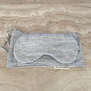 Linen sleep mask with its pouch in soft ivory/black pinstripes, displayed on a kitchen counter.