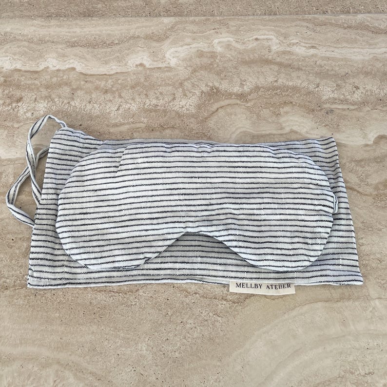 Linen sleep mask with its pouch in soft ivory/black pinstripes, displayed on a kitchen counter.