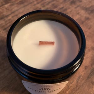 Amber glass jar scented coco soy wax candle on a table showing a closeup of the wax and the wood wick from above.