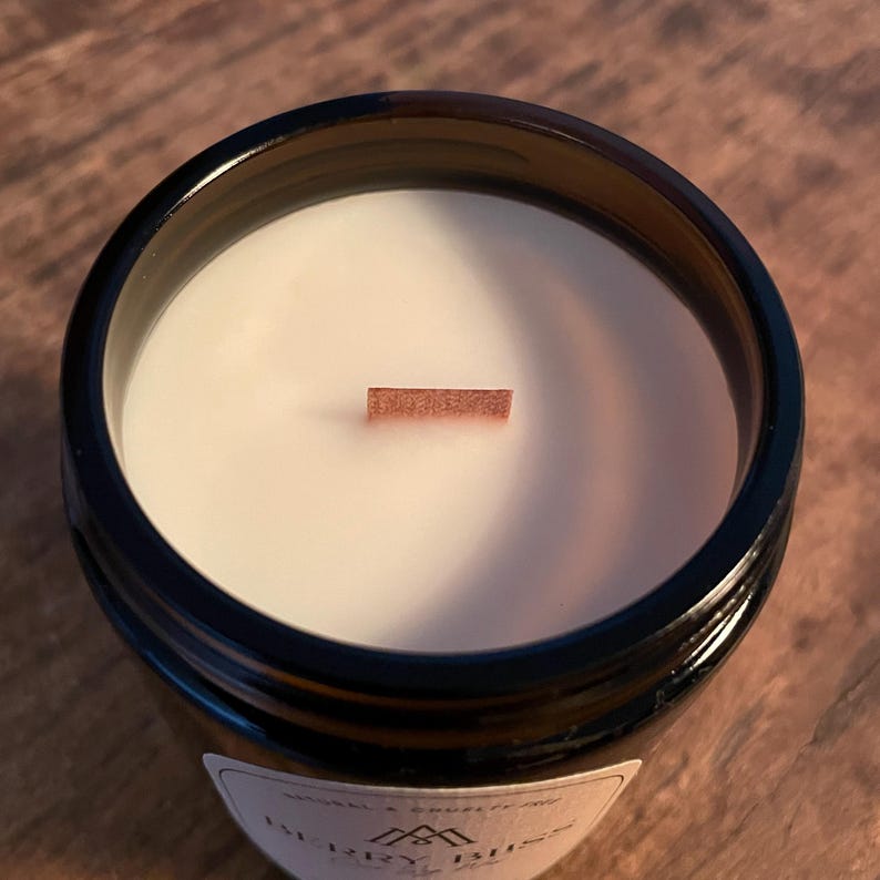 Amber glass jar scented coco soy wax candle on a table showing a closeup of the wax and the wood wick from above.