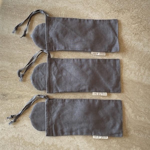 Three charcoal grey sleep masks peeking out of their drawstring pouches, displayed on a kitchen counter.