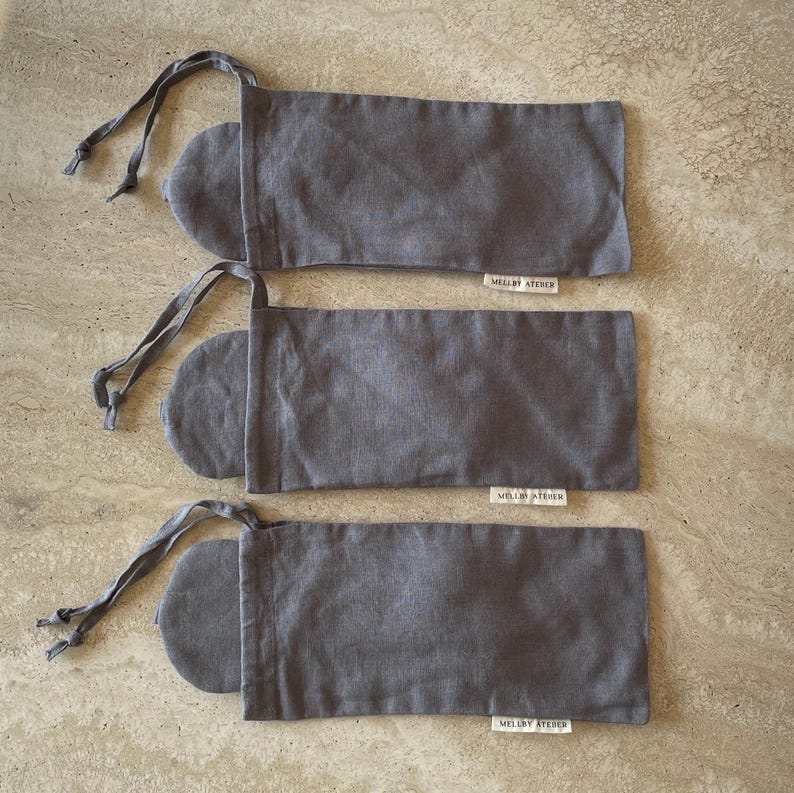 Three charcoal grey sleep masks peeking out of their drawstring pouches, displayed on a kitchen counter.