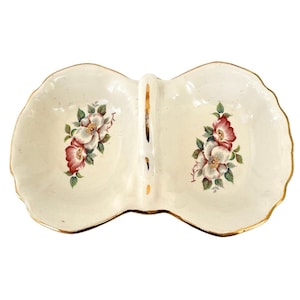 May include: A white ceramic double dish with a gold rim and floral design. The dish has a handle in the center and is perfect for serving snacks or appetizers.