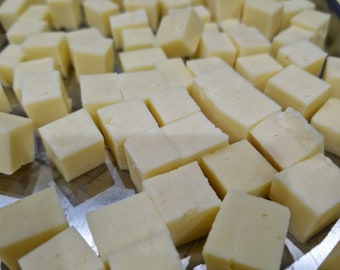 May include: A close-up shot of a tray filled with numerous small, evenly cut cubes of cheese. The cheese is a pale yellow color, and the cubes are uniform in size and shape. The cubes are scattered across the tray.