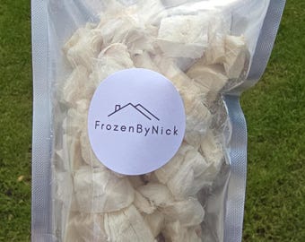 May include: A clear plastic bag filled with light-colored, irregularly shaped food items. A white circular label with a house and mountain graphic and the text "FrozenByNick" is affixed to the bag. The bag is held against a green grassy background.