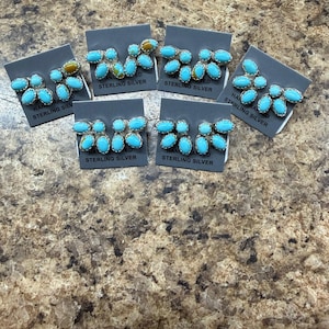 May include: Six pairs of handcrafted sterling silver earrings with turquoise stones. Each earring set features a cluster of oval-shaped, bright blue stones set in a silver frame. The earrings are displayed on gray cards with the text "STERLING SILVER".