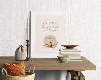 May include: A framed print with the text "Her children rise up and call her blessed" and "Proverbs 31:28". The print is decorated with floral elements. A candle, books, and a decorative basket are on a wooden table.