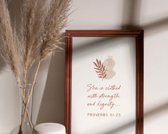 May include: A framed print with the text "She is clothed with strength and dignity... PROVERBS 31:25" in a brown frame. Beside it is a vase with dried pampas grass and a white ceramic jar.