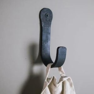 Puede incluir: Un gancho de metal negro montado en una pared con un paño blanco colgando de él.