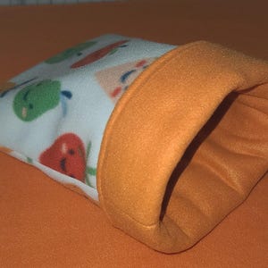 May include: A small, cone-shaped pet bed with a white exterior patterned with colorful fruits and vegetables. The bed has an orange rim and interior, and is likely made of soft fleece material.
