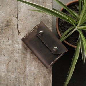 Taupe crazy horse leather wallet in closed position displaying two brass snap fasteners securing the fold-over flap. Rectangular minimalist design with smooth matte finish and subtle pull-up effect where leather shows lighter tones from handling.