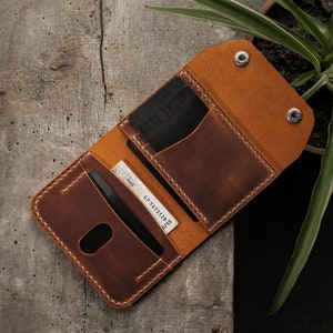 Hand demonstrating open wallet interior layout with cards inserted in slots and folded banknote in center compartment. Six dedicated card slots visible with easy-access thumb notches. Scale shows pocket-friendly size when held in adult hand.
