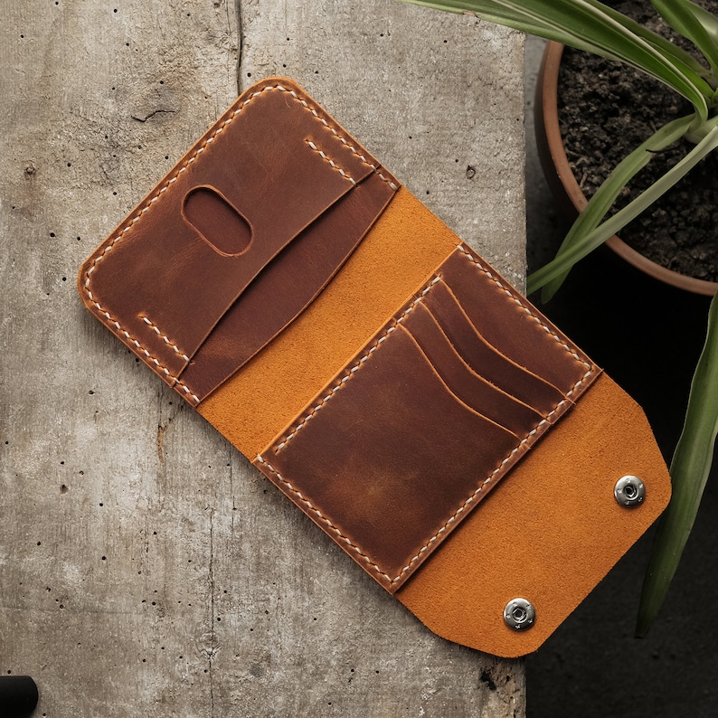 Open crazy horse leather wallet in camel color resting on white surface, showing interior compartment layout with six card slots and central cash pocket. Light camel-colored leather lining contrasts with darker exterior. Hand-stitched construction with waxed thread visible along edges.