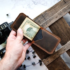 May include: A brown leather wallet with a money clip and a ten dollar bill inside. The wallet is open and the bill is visible.