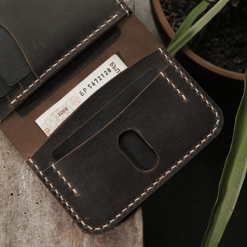 Close-up macro view of card slot with oval thumb notch cutout in taupe crazy horse leather. Detail shows hand-stitched seam construction and the distinctive waxy surface texture that characterizes this leather treatment and finishing process.